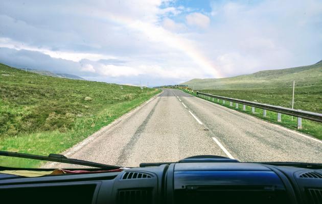 Open road in Scottish Highlands with a rainbow in the background.