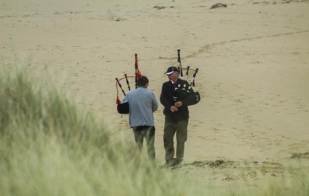 Two men standing on a beach playing bagpipes