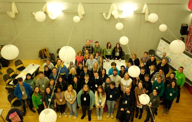 Around 70 youth delegates stand together in a room for camera