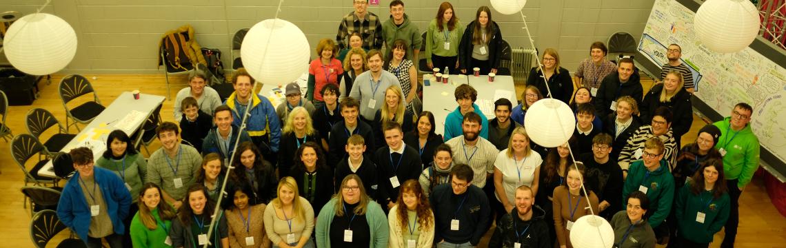 Around 70 youth delegates stand together in a room for camera